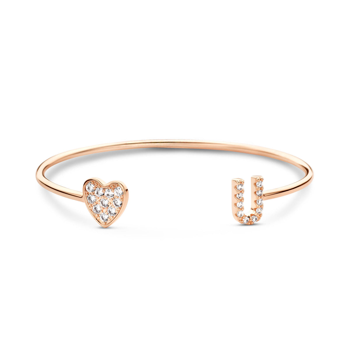 Een open rosékleurige armband met een glinsterend hartje en een letter op wit.